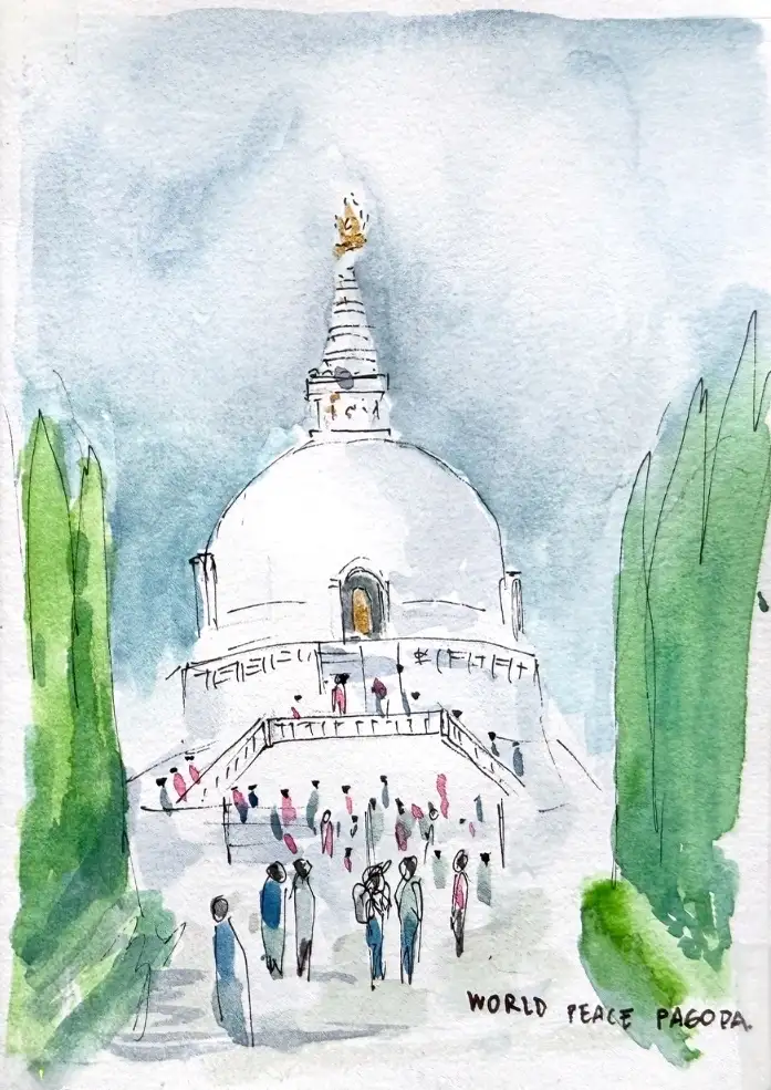 The World Peace Pagoda, a white dome with a gold finial, a crowd climbing the steps towards it, framed by two dark cypress trees